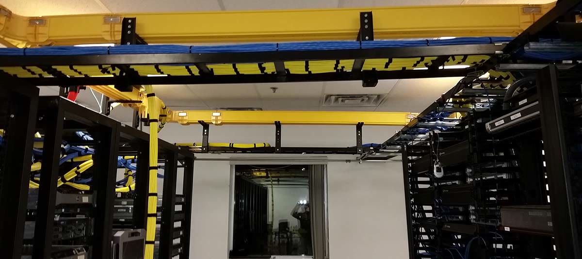 A wide data-room shot with yellow cable ladder trays feeding racks on both sides